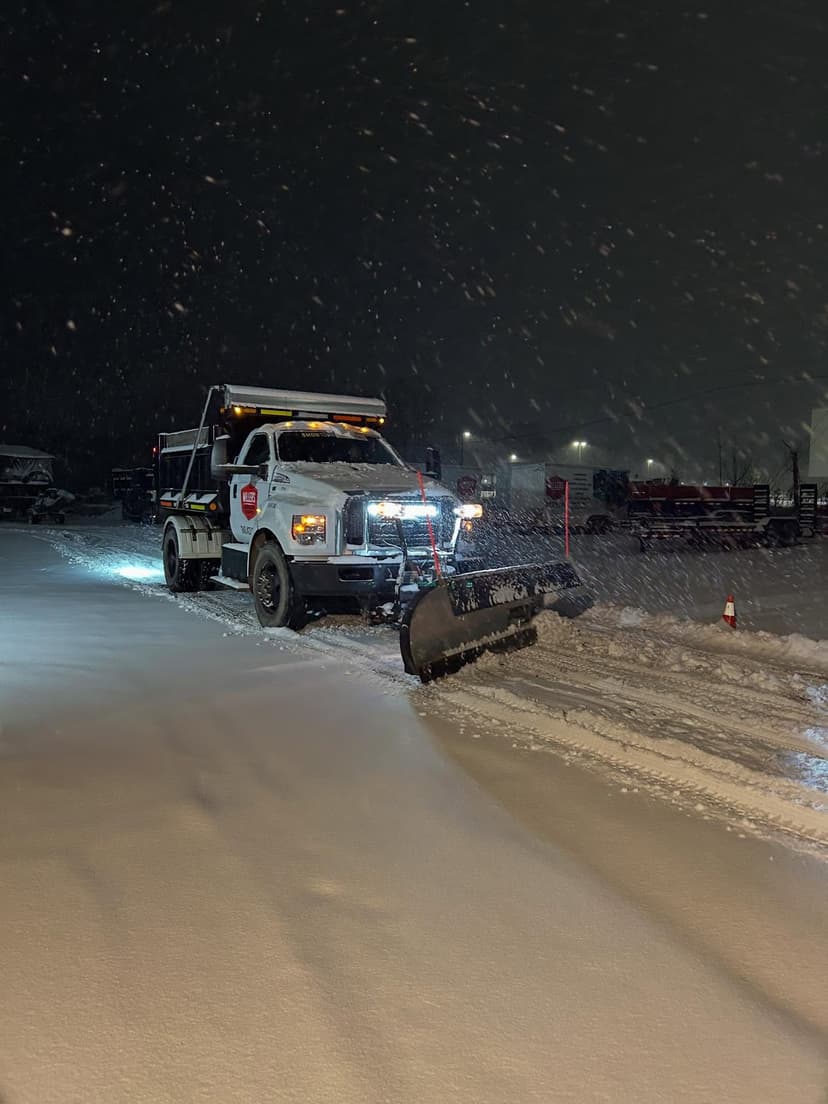 Snow plow truck clearing snow in a parking lot during a snowstorm at night.